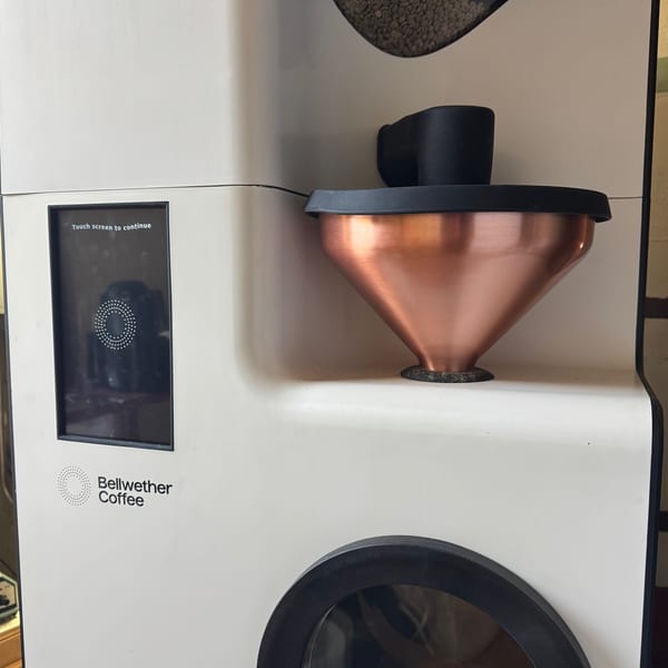 A Bellwether Coffee roaster with a copper funnel and a screen displaying "Touch screen to continue".