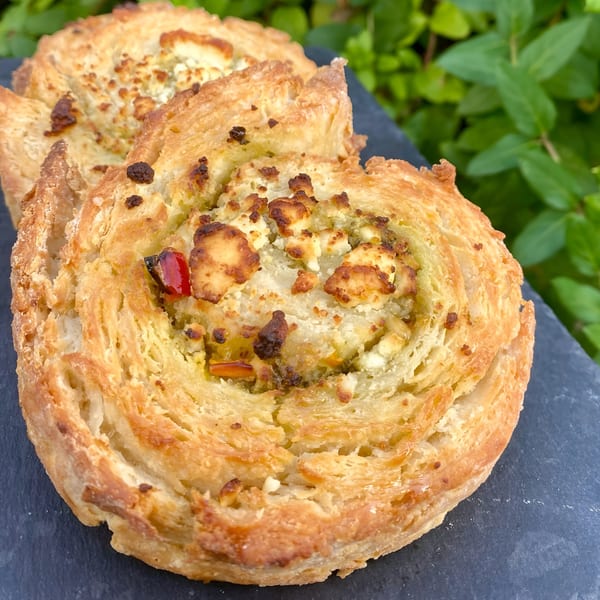 Two golden-brown savory pastries with cheese and red pepper, on a dark slate board.