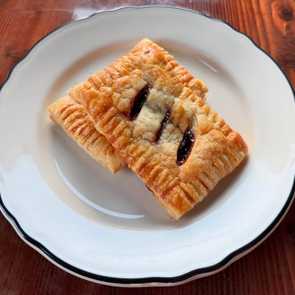 Two golden-brown Riv Cafe pastries with fruit filling and sugar on a white plate.