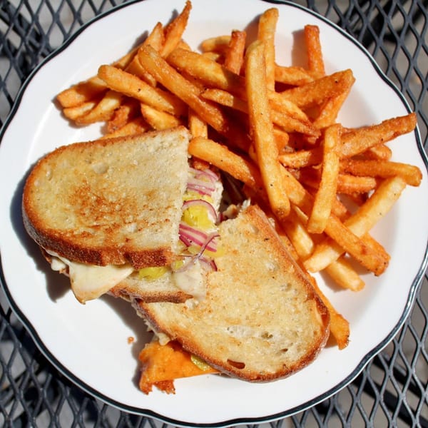 A grilled cheese sandwich with red onions and pickles, served with golden french fries on a white plate.
