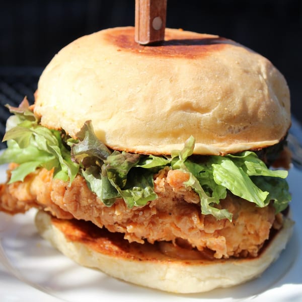 Crispy fried chicken sandwich with fresh green lettuce on a toasted bun from The Riv Cafe.