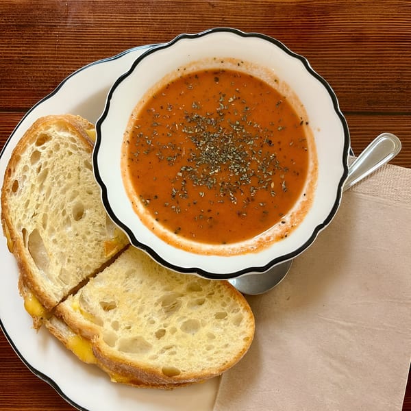 A bowl of tomato soup with herbs and a grilled cheese sandwich on a white plate.