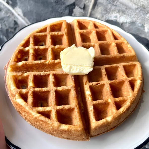 Golden-brown waffle with a pat of butter on a white plate at The Riv Cafe.